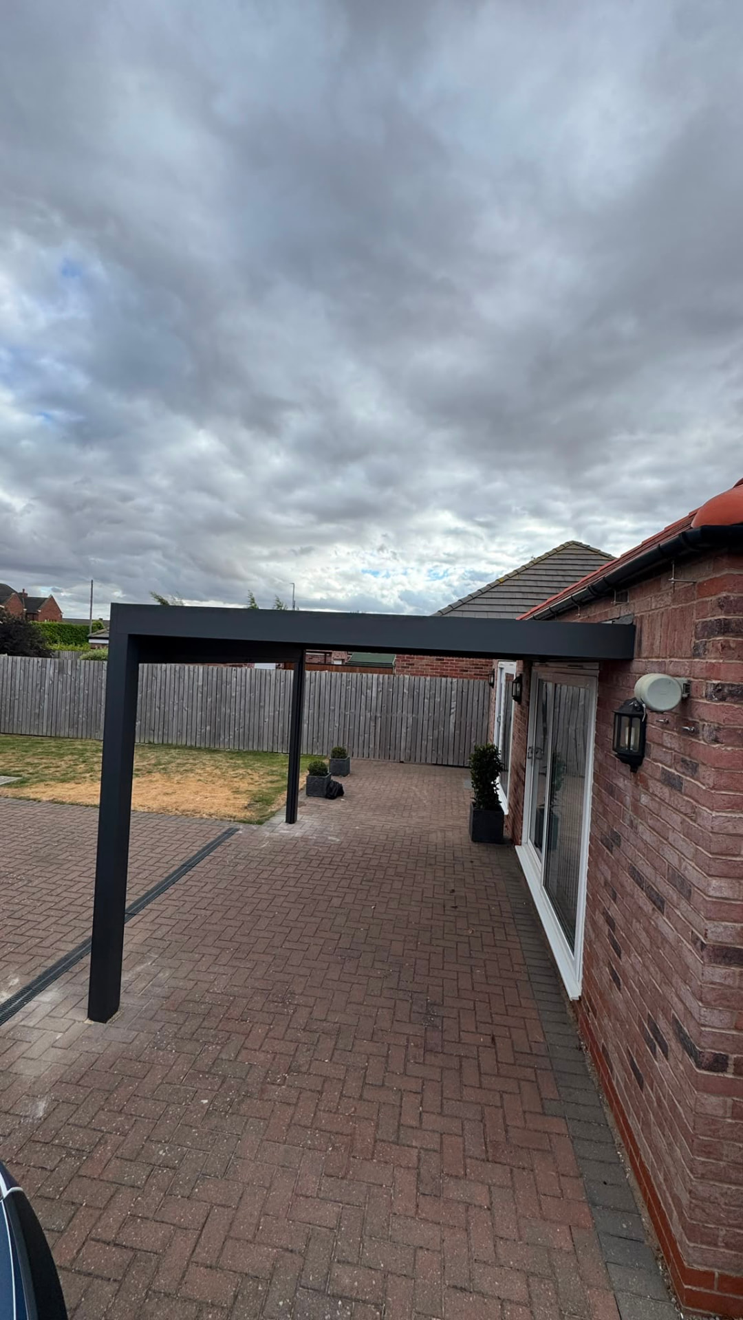 Aluminium carport frame over a block paved driveway beside a bungalow